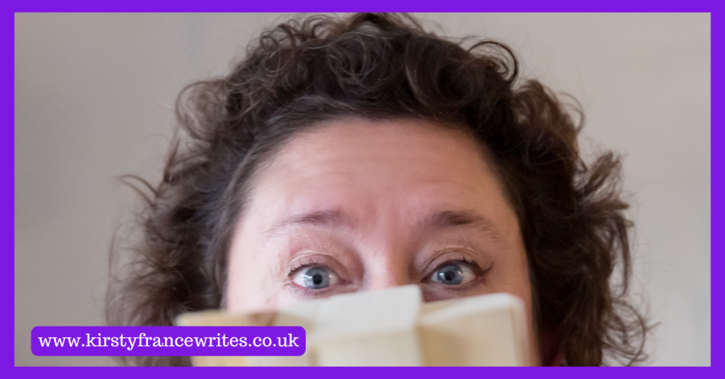 Image shows a women with dark curly hair and blue eyes hiding the rest of her face behind books. She's thinking about her marketing voice.